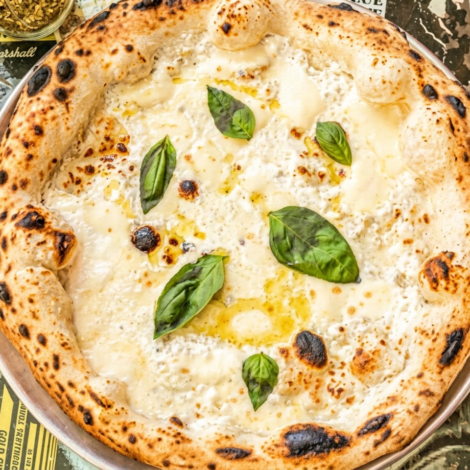Neapolitan-style white pizza topped with melted cheese, ricotta, olive oil, and fresh basil on a metal plate.